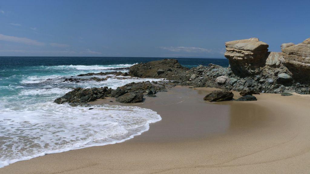An ocean wave spills onto a mixed sandy and rocky shore.