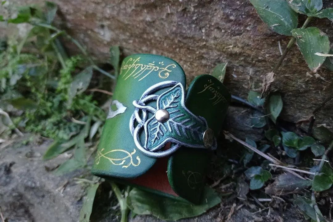 More focused pic of the fastener, partially at shadow. It's a Lórien leaf, like the elven brooches received by the Fellowship, with the border and filigrees in metallic silver and the rest of the leaf painted in metallic shiny green, attached to the cuff by silver rivets