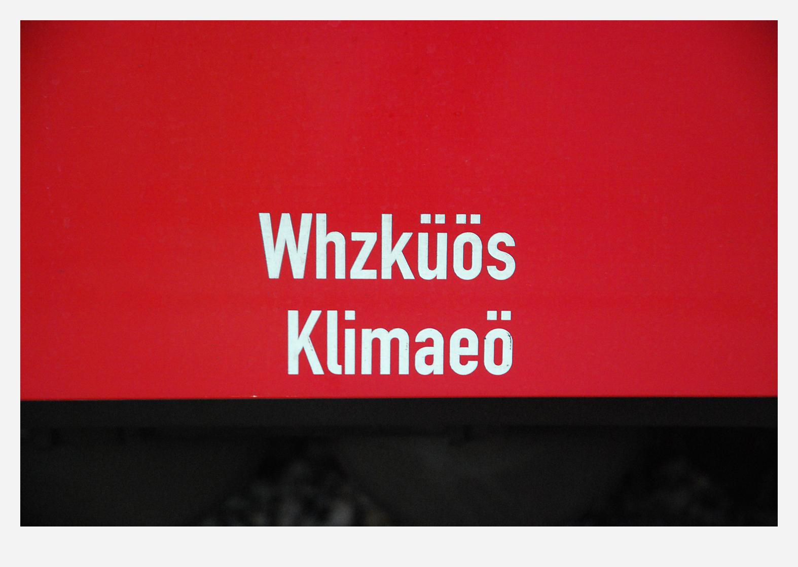 Close-up of an inscription on a red railway vehicle. In white letters it says:
Whzküös
Klimaeö