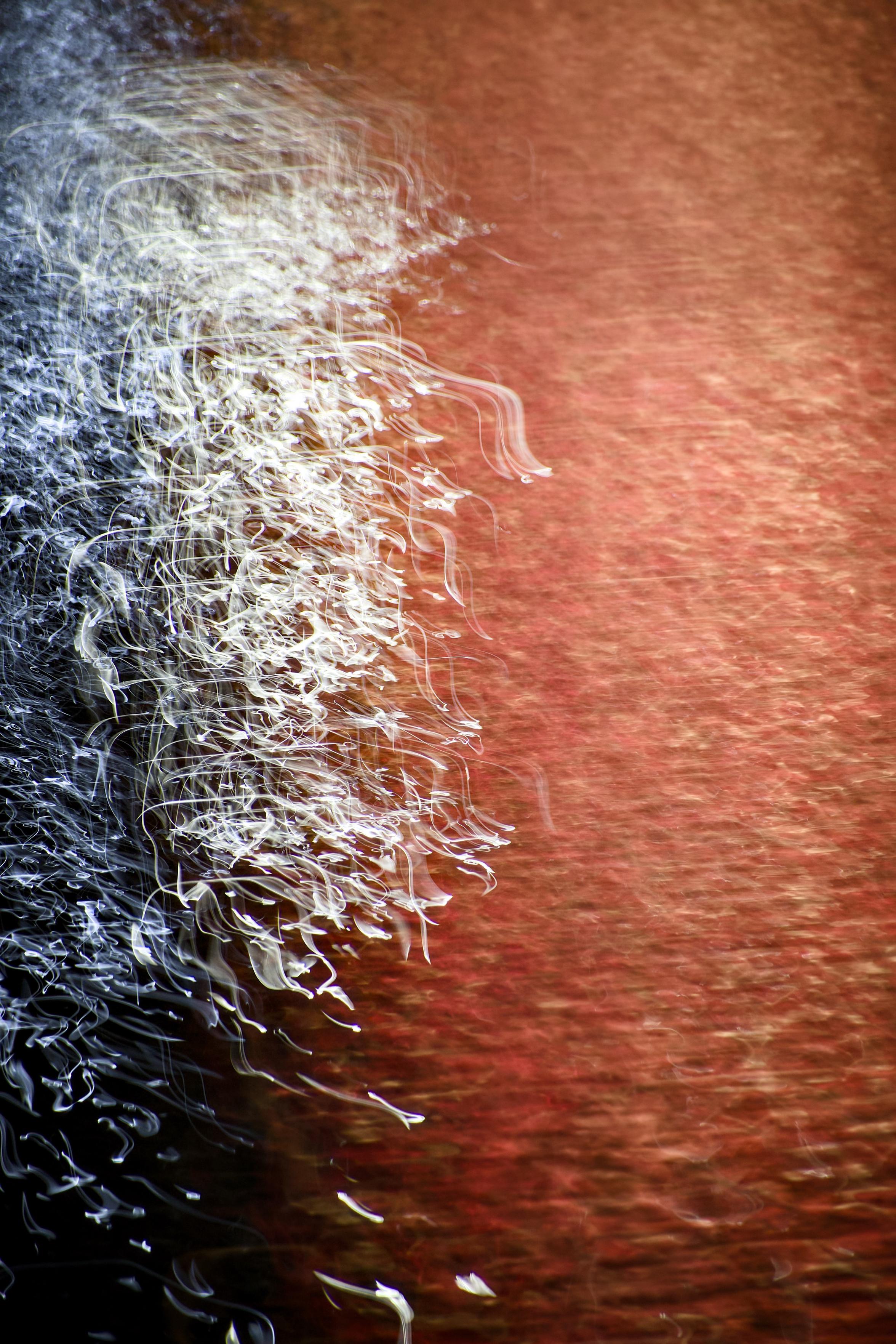 Abstract image showing the reflections of red and bright white lights on the surface of the River Clyde at night, where a 1-second exposure and intentional camera movement has created abstract patterns.