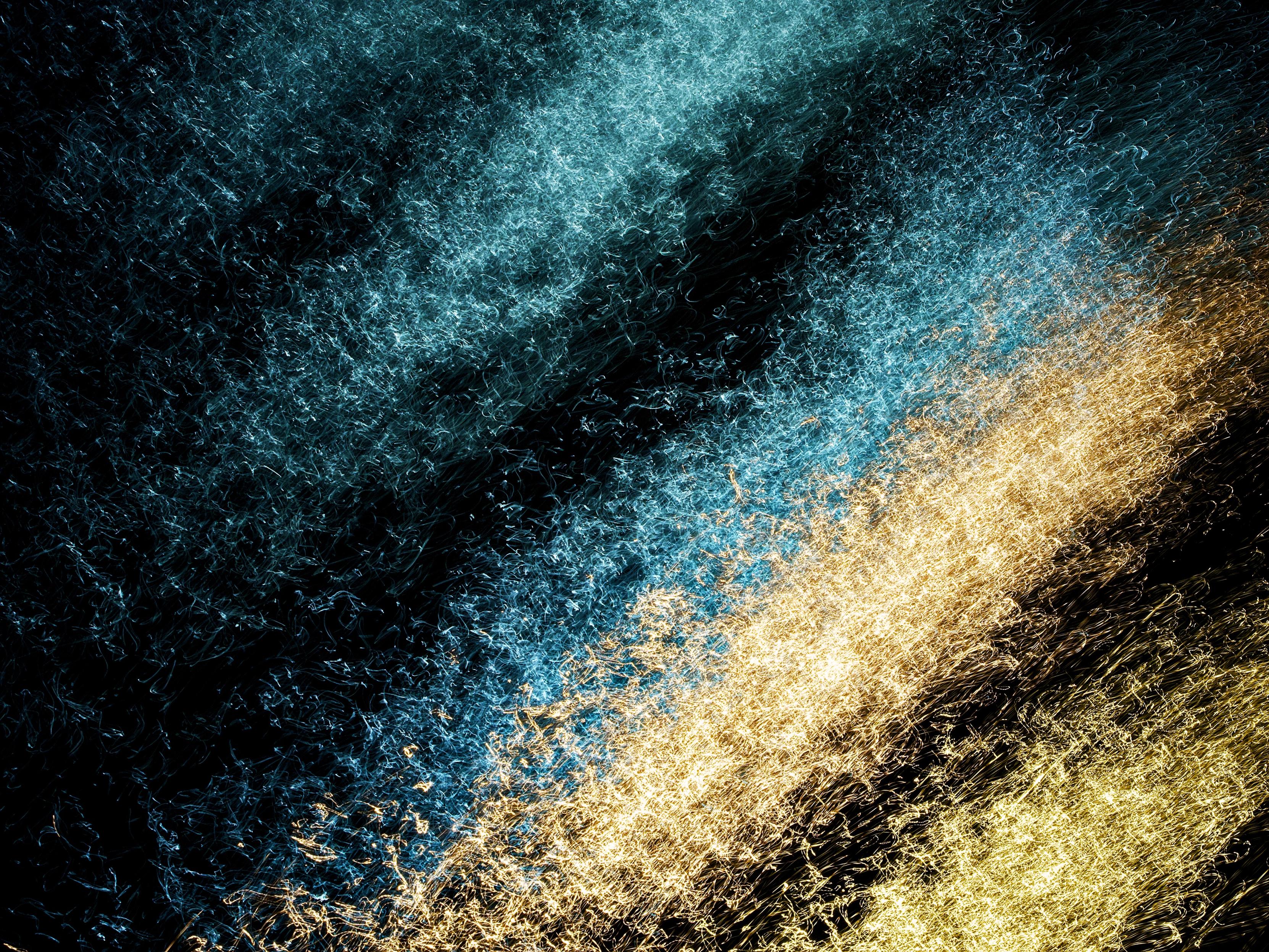 Abstract image showing the reflections of turquoise and golden yellow neon lights on the surface of the River Clyde at night, where a 1-second exposure and intentional camera movement has created abstract patterns.
