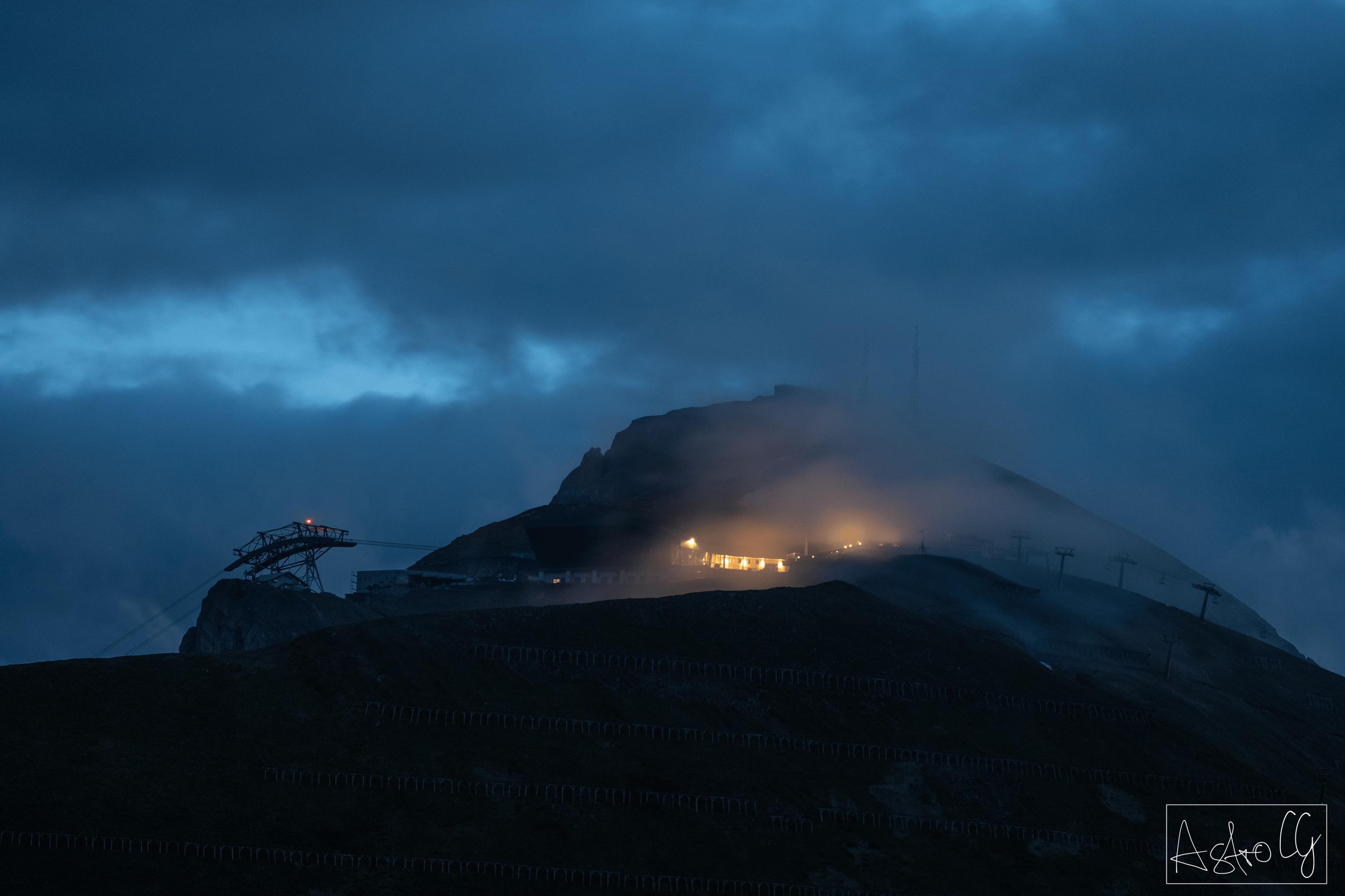 Mountain peak at night with illuminated mountain station and fog