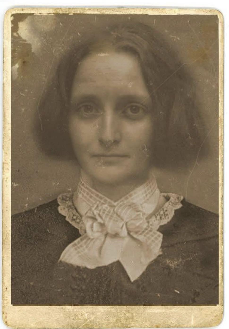 A vintage, sepia-toned photo of a woman with shoulder-length hair, wearing a dark dress and a large bow tie. The image has a worn texture and slight imperfections, reflecting its age. Apparently the only existing photo of Mary Shelley
