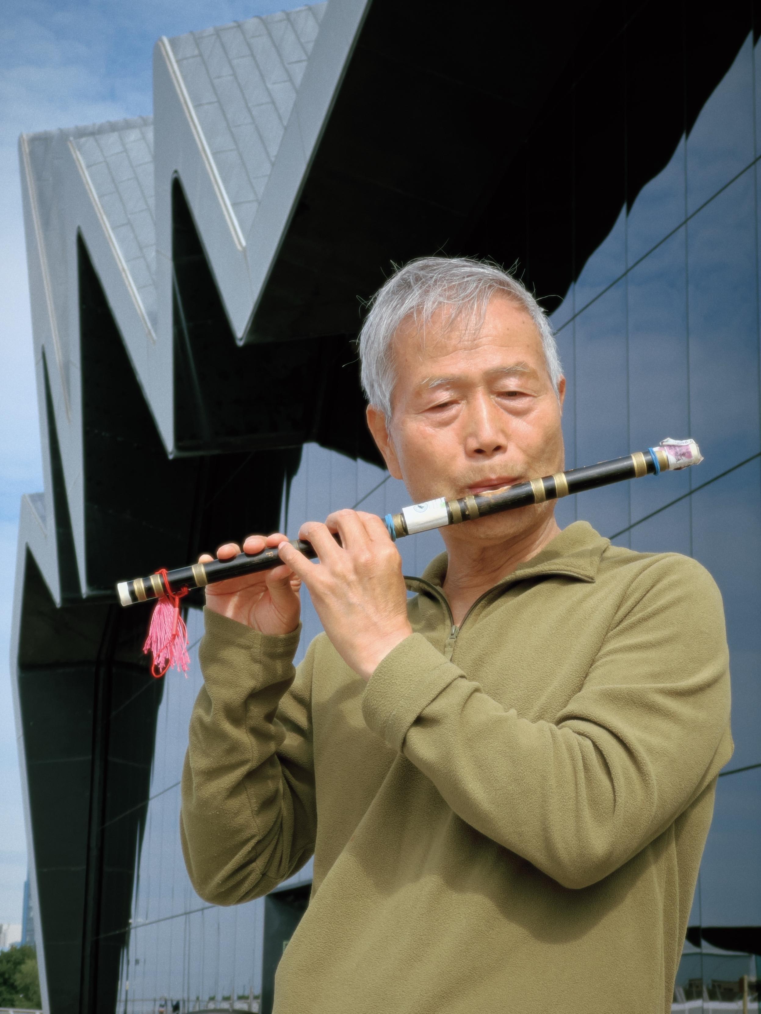 Gao Xijing playing his traditional Chinese flute, something he does all around Glasgow just for pleasure, outside the Riverside Museum on the banks of the Clyde