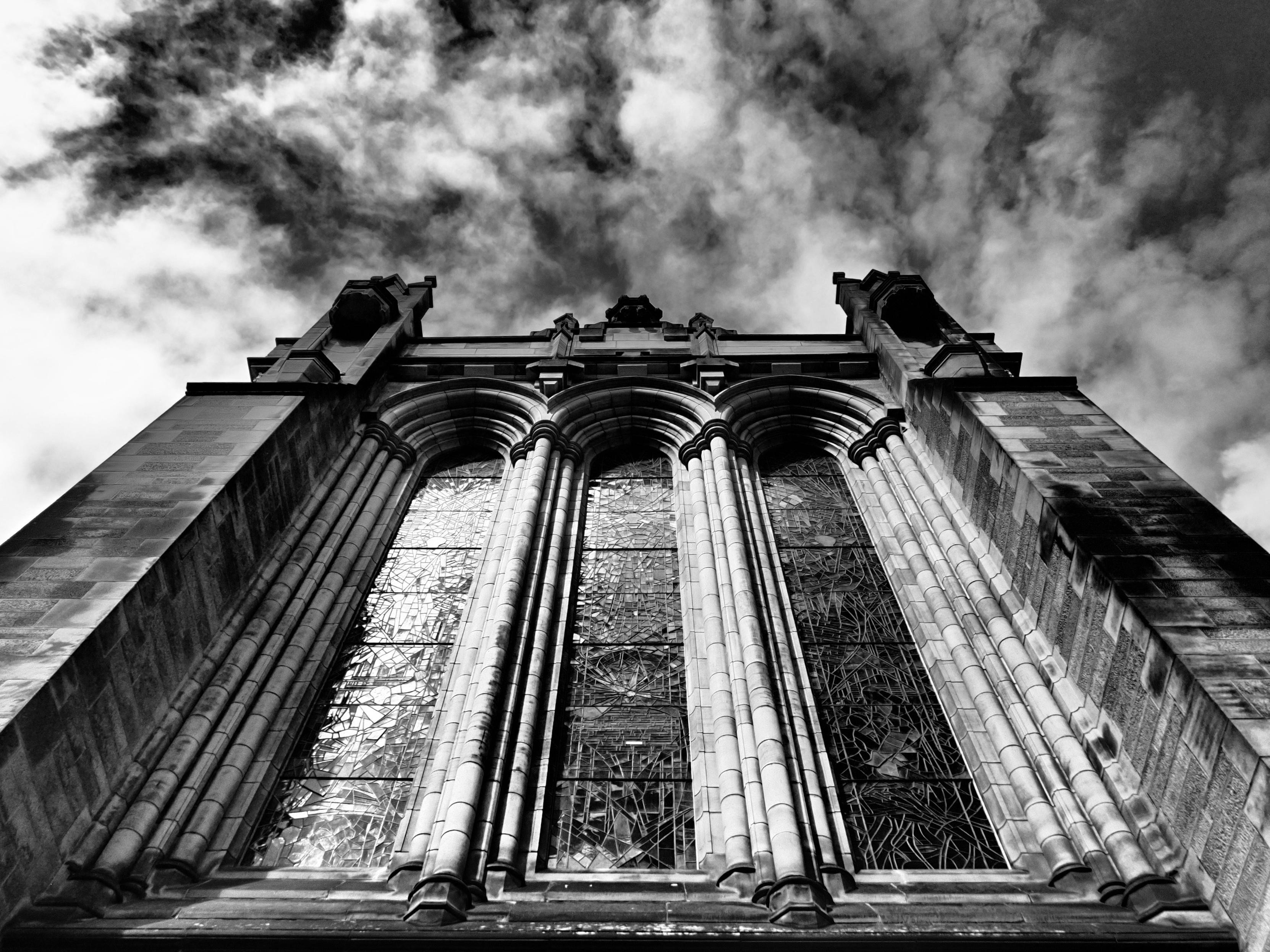 Looking upward toward soft, white clouds in a dark blue sky, beneath the three ornate leaded windows of the Glasgow University chapel.