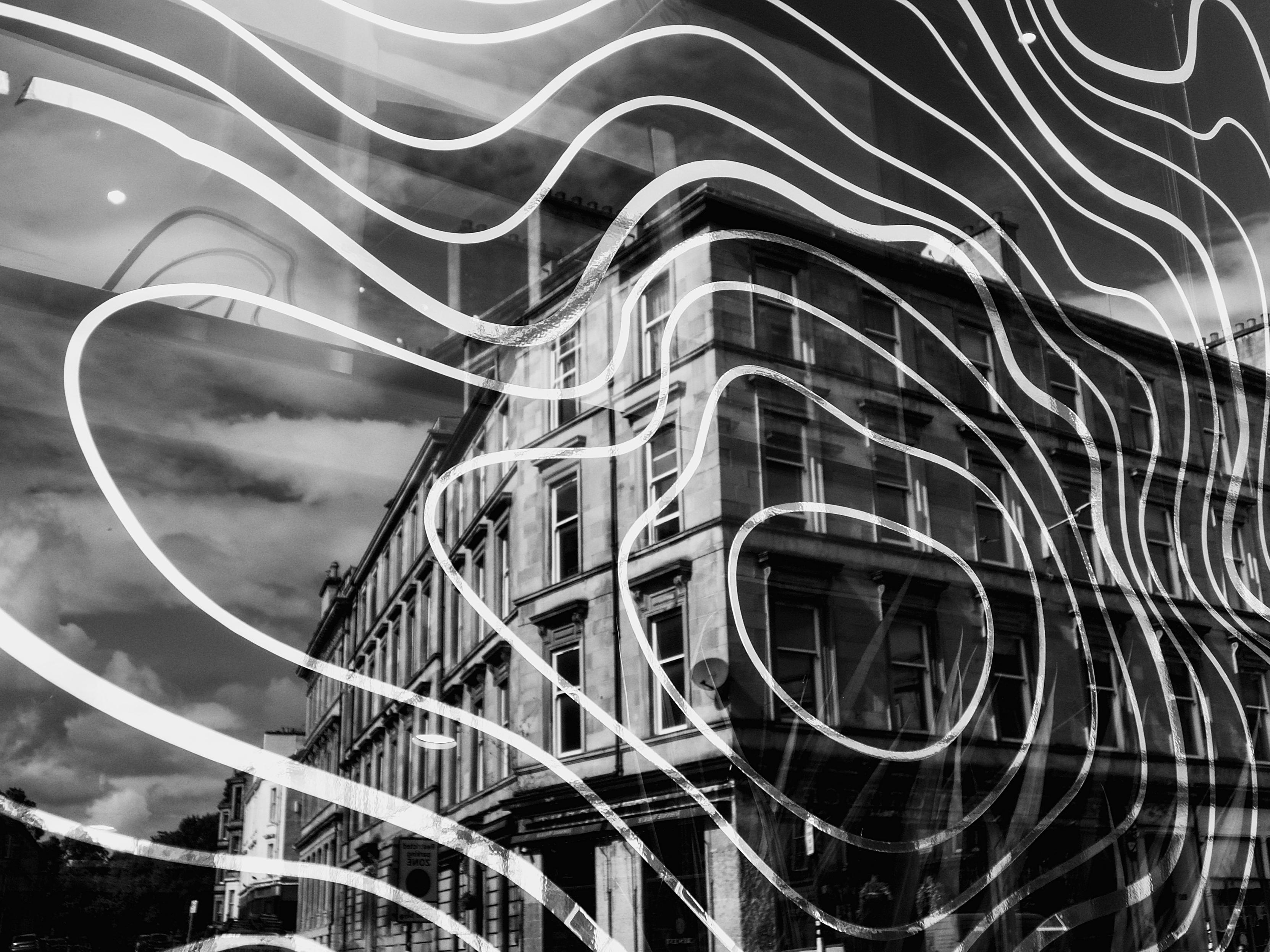 Ornate, swirling golden patterns etched on a restaurant window which is reflecting the stone tenement building across the road in Finnieston.