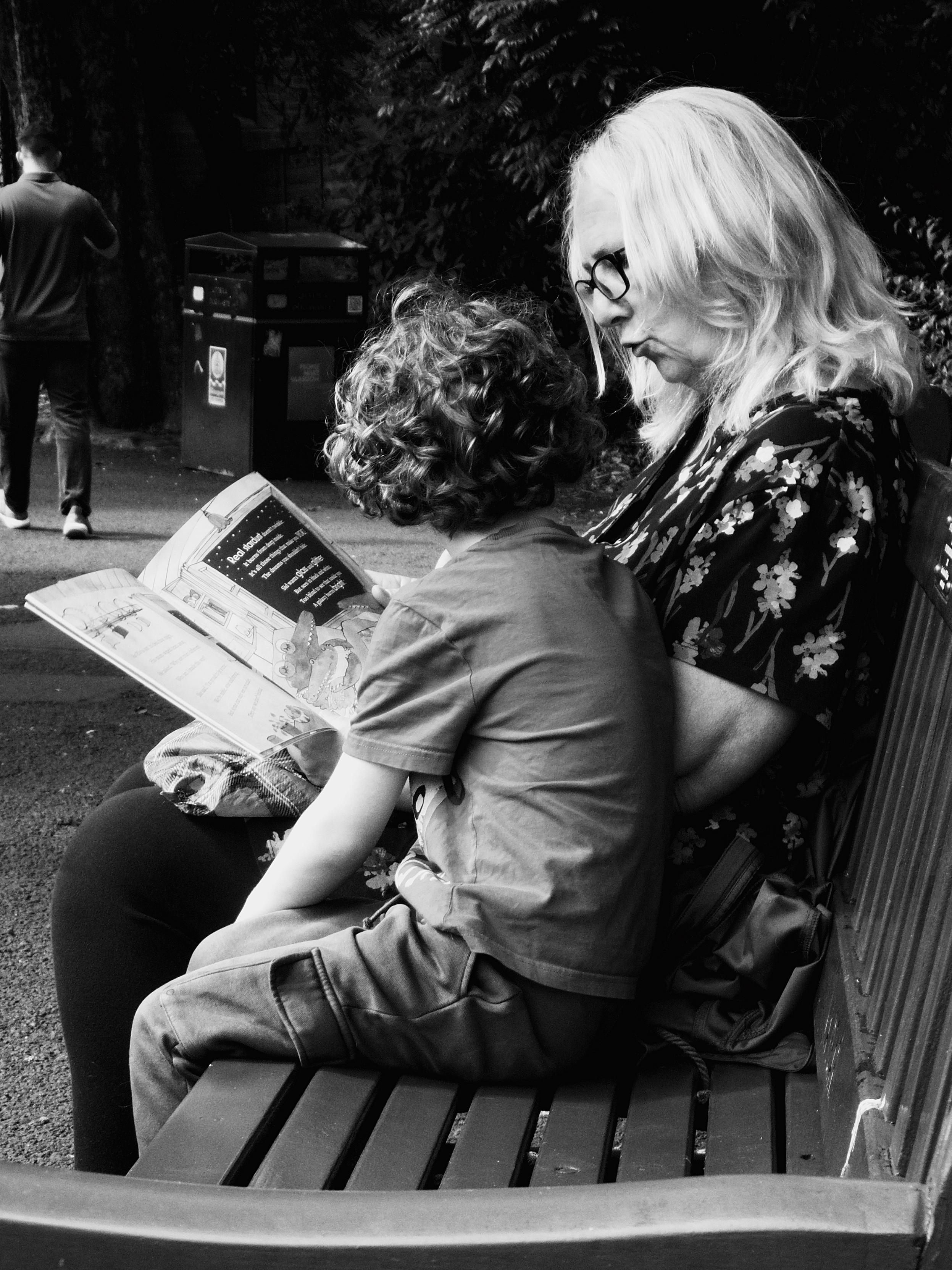A gran reads out loud to her grandson while sitting on a bench in the sunshine in Glasgow's Botanic Gardens
