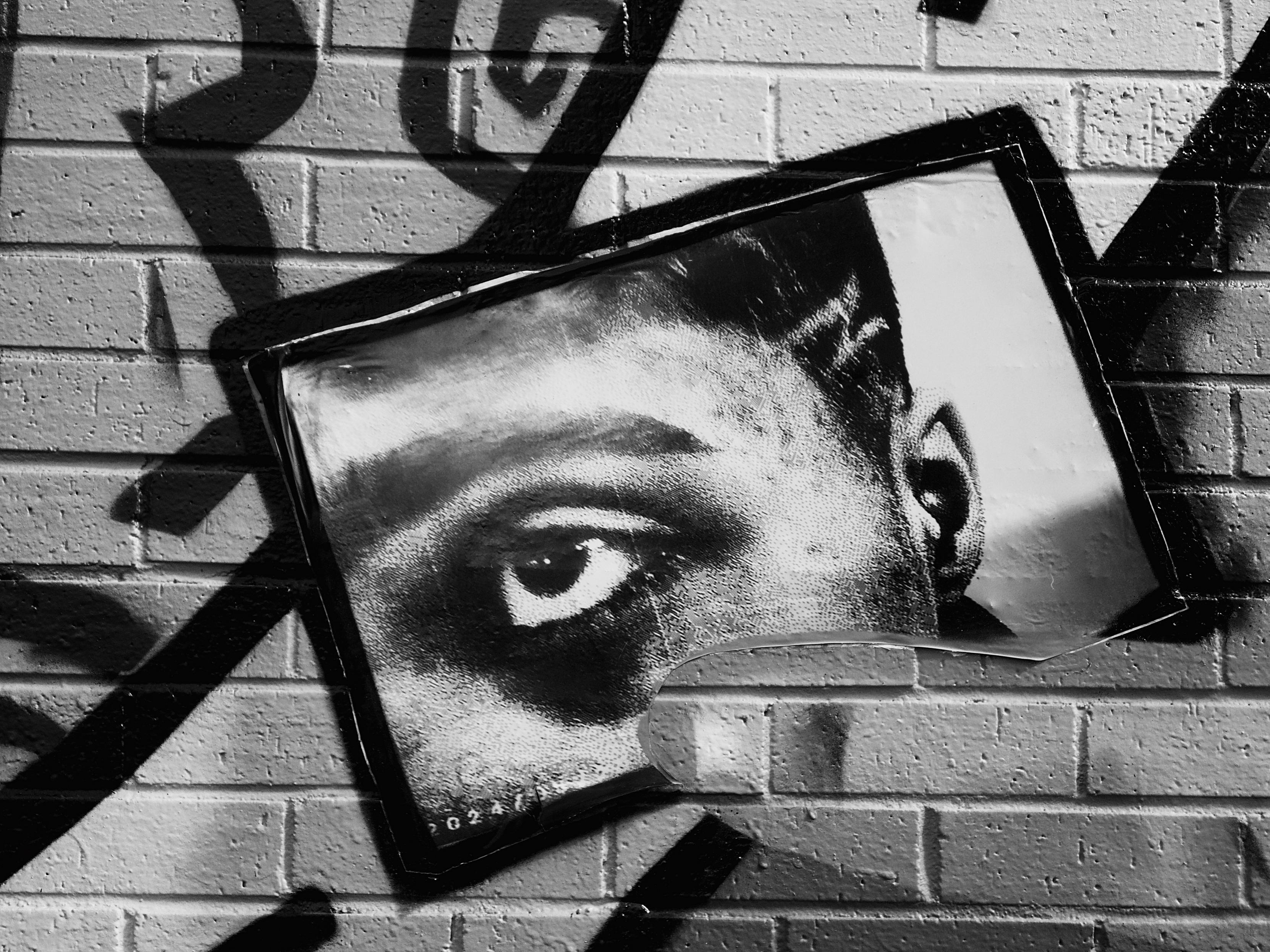 Image shows part of a street art piece in the Yardworks archways area in Finnieston, with a torn print of a close-up of a man's eye surrounded by thick black lines and spray-painted designs. The eye is very commanding in its gaze.