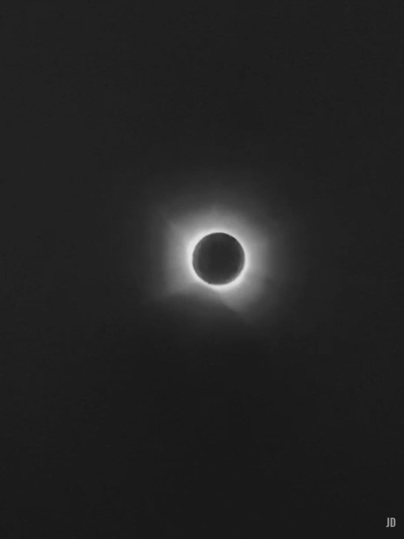 La imagen muestra un eclipse solar total, con la Luna cubriendo completamente el Sol y dejando visible la corona solar como un halo brillante alrededor del disco oscuro. El fondo es completamente negro, destacando el contraste entre la sombra de la Luna y el resplandor solar.
