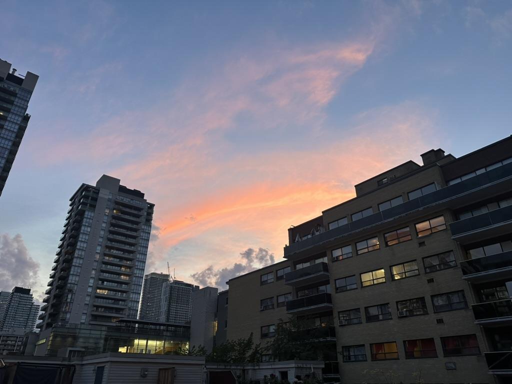 Downtown city skyline from within showcasing a darkening sky with backlit clouds and and orange arc of sunset almost like a rainbow.