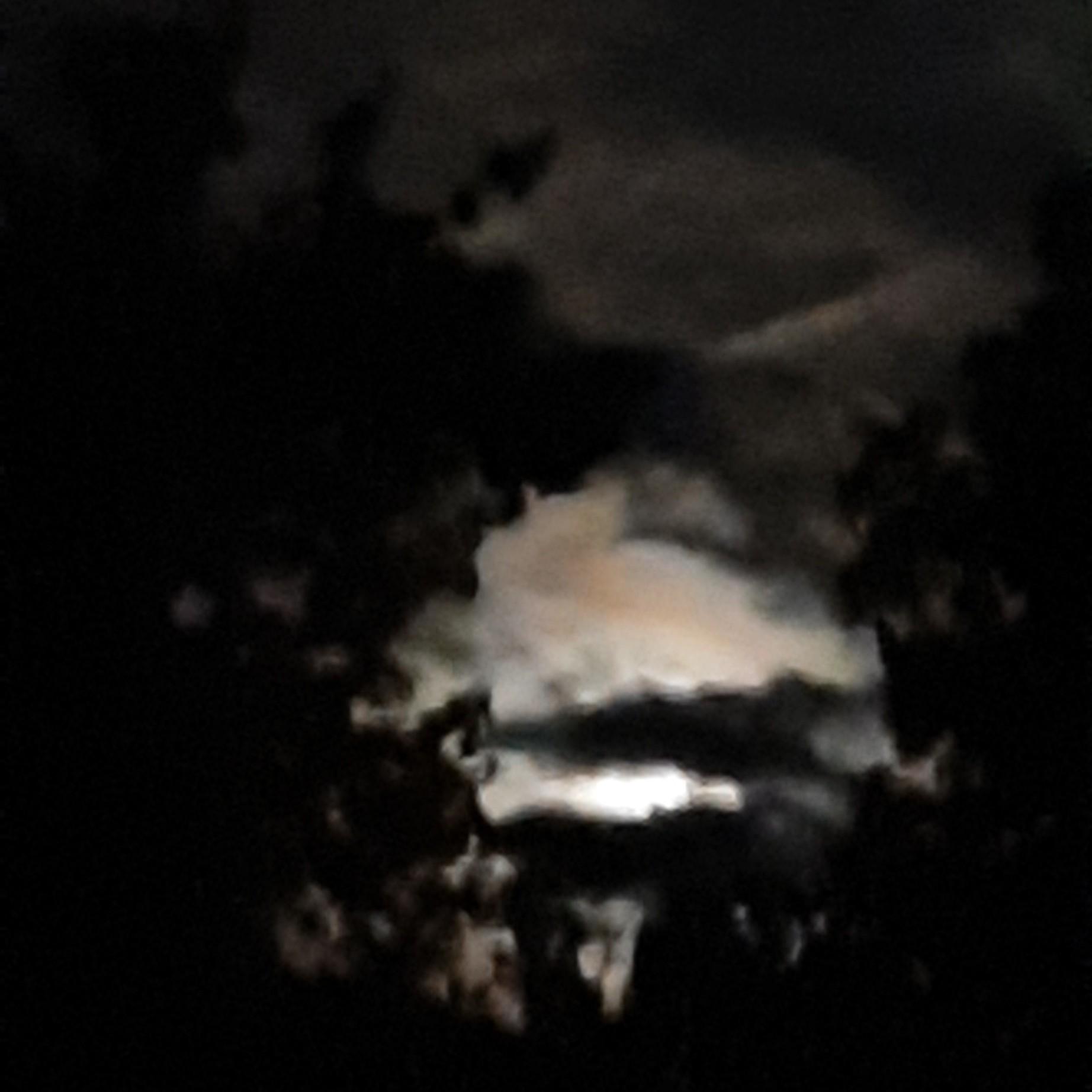 a square photo of lights in the sky, behind black clouds. Just some blurry orange with white