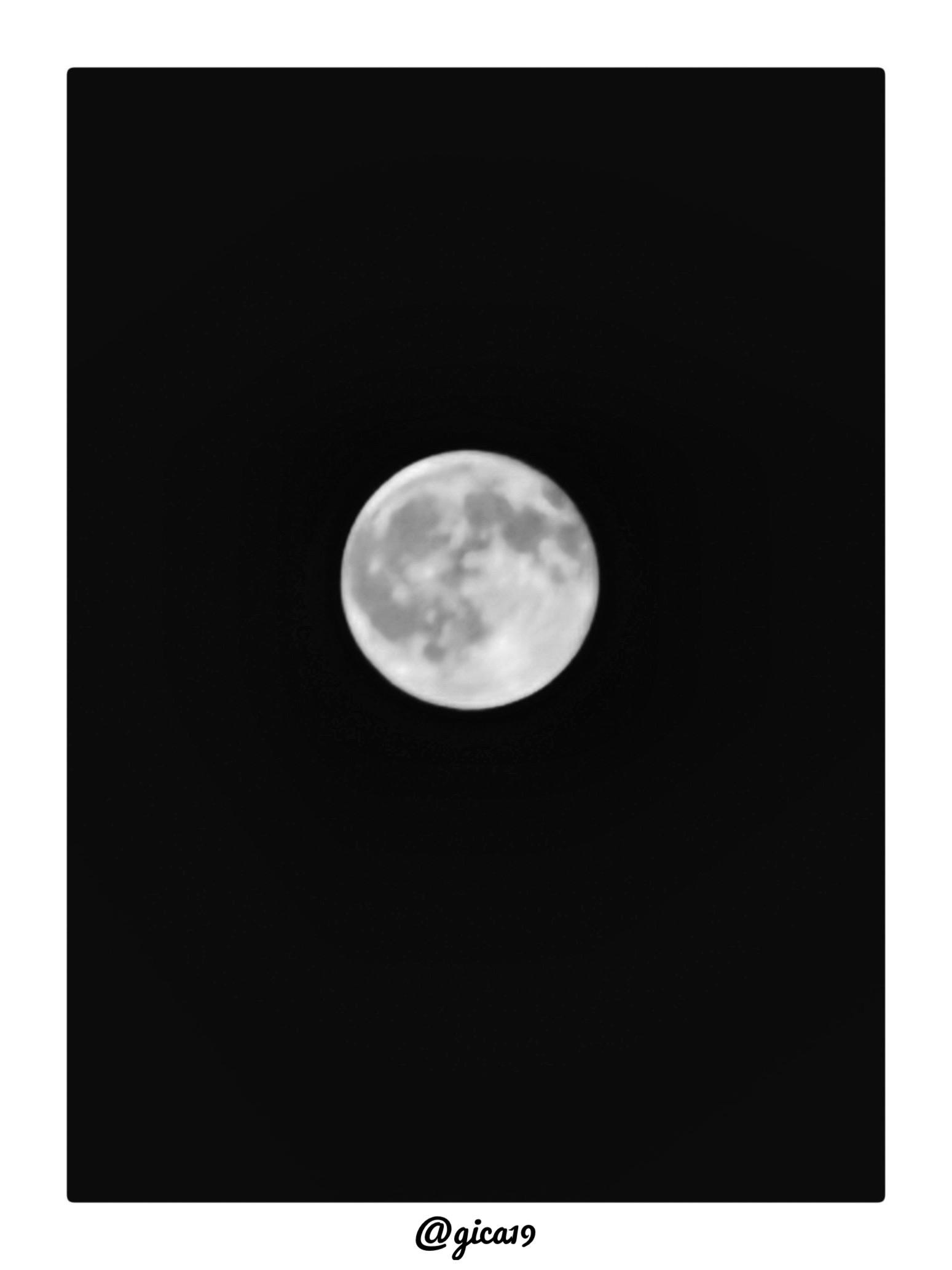 La imagen muestra una fotografía de la Luna llena captada de noche, con el fondo completamente negro que resalta el disco lunar en tonos grises y blancos. Se aprecian con claridad los mares lunares (las zonas oscuras) y las regiones más claras de la superficie, lo que sugiere una toma con teleobjetivo o zoom óptico considerable para lograr ese nivel de detalle en los cráteres y accidentes geográficos. La composición está centrada, con la Luna ocupando aproximadamente un tercio del encuadre vertical, dejando un amplio espacio negro alrededor que refuerza el contraste.