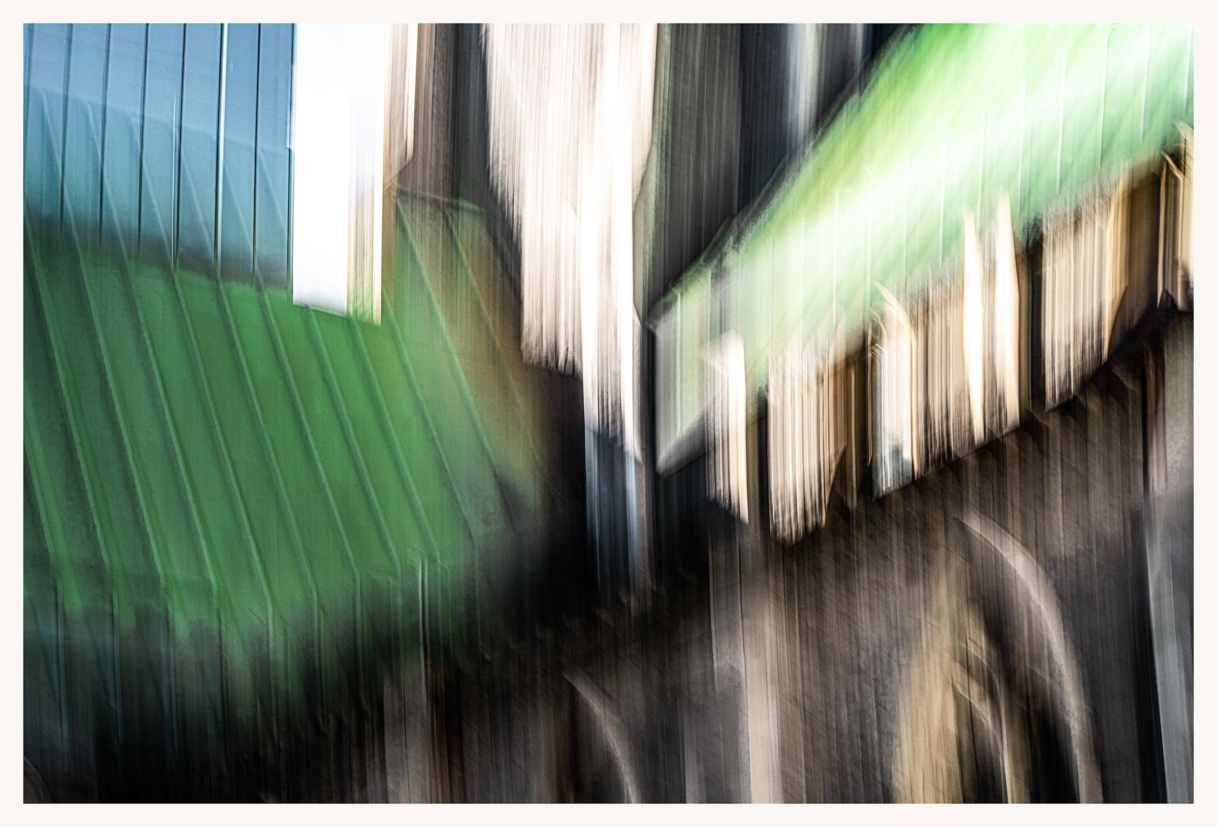 A blurry intentional camera movement photo of the green metal rooftop of Christchurch Cathedral in Montreal. At the top left, the green melts into the blueish glass windows of a modern structure. At the bottom of the image, the roof melts into the brownish stone of the church and its arched Gothic windows. It looks as though a mysterious dark figure is looking out of one of the windows, but it's just a ghostly artifact. Or is it???